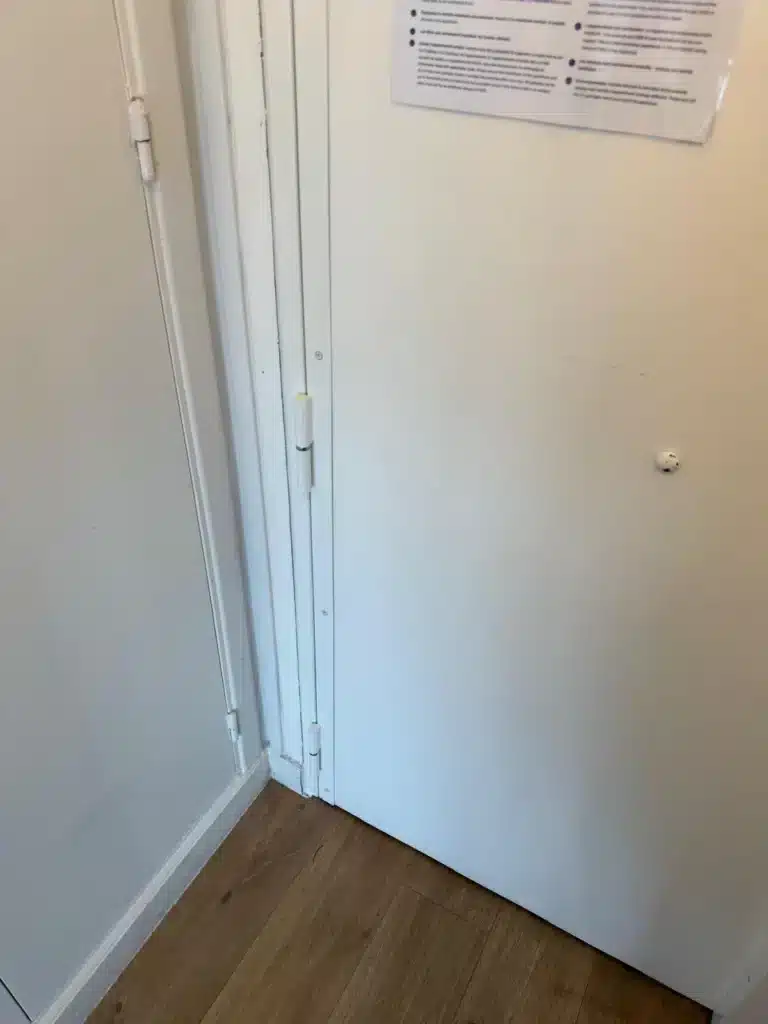 Porte blindée blanche posée dans un appartement, vue de l'intérieur, poignée et paumelles visibles