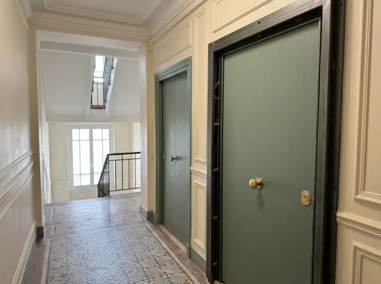 Porte blindée vert sauge sur un palier commun, assortie à la porte voisine et aux moulures existantes.