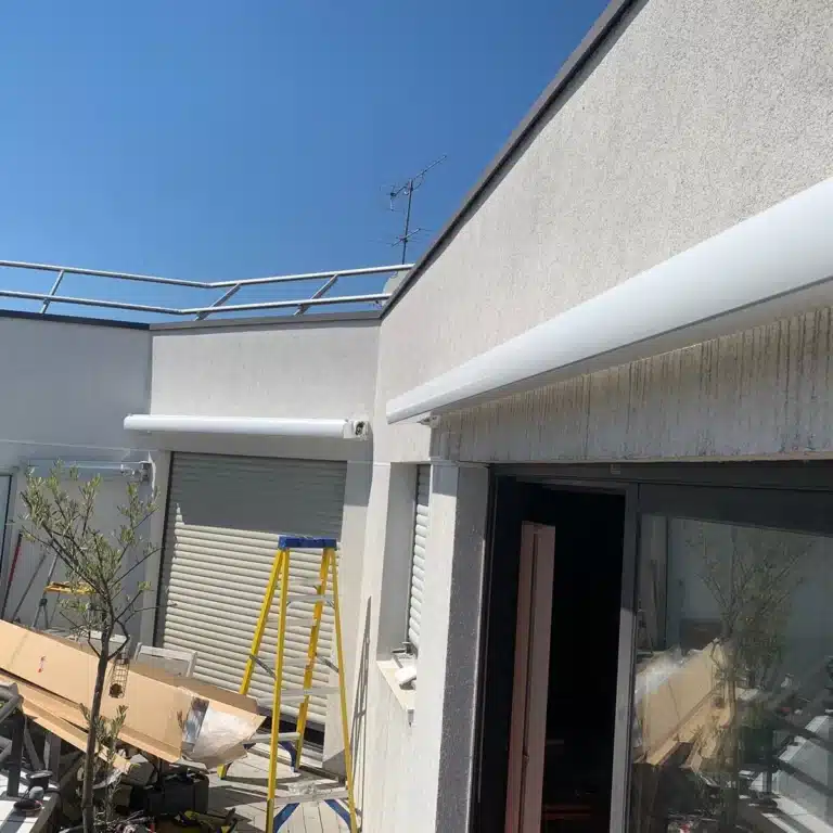 Store banne coffre blanc fixé en façade au-dessus d'une baie vitrée, vue en contre-plongée