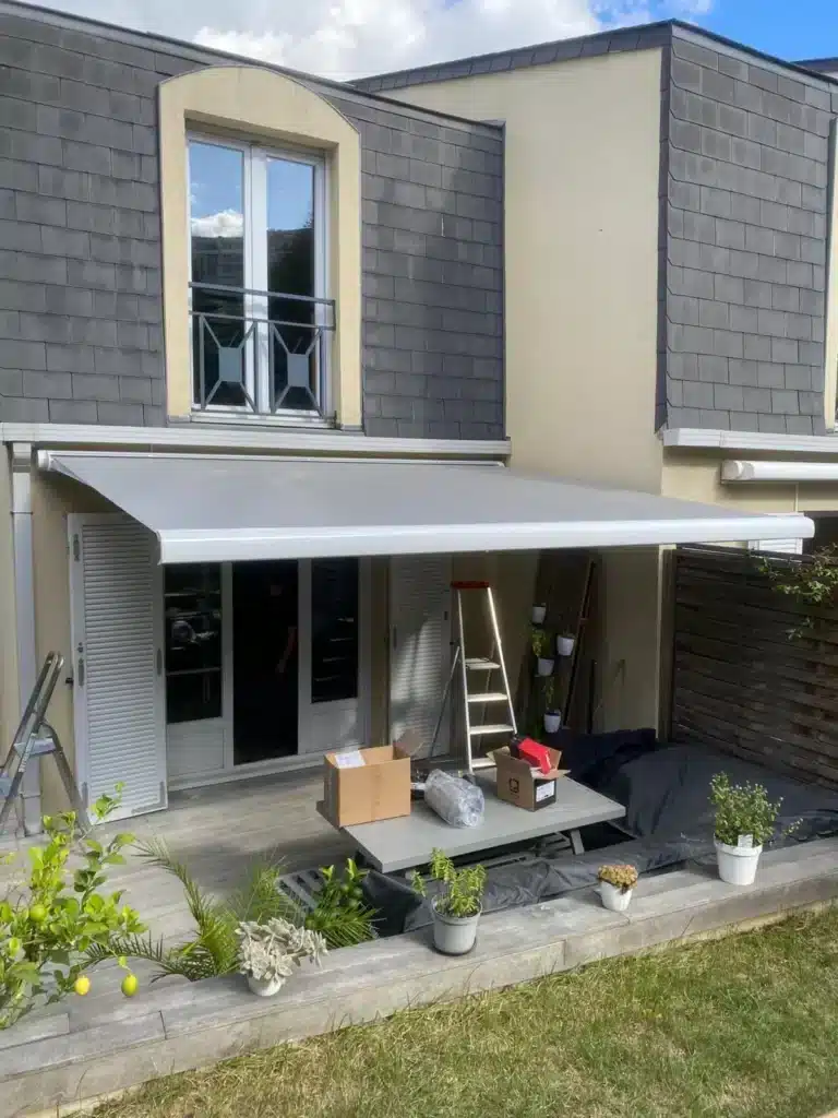 Store banne gris déployé au-dessus d'une terrasse de maison, cartons d'emballage au sol après la pose