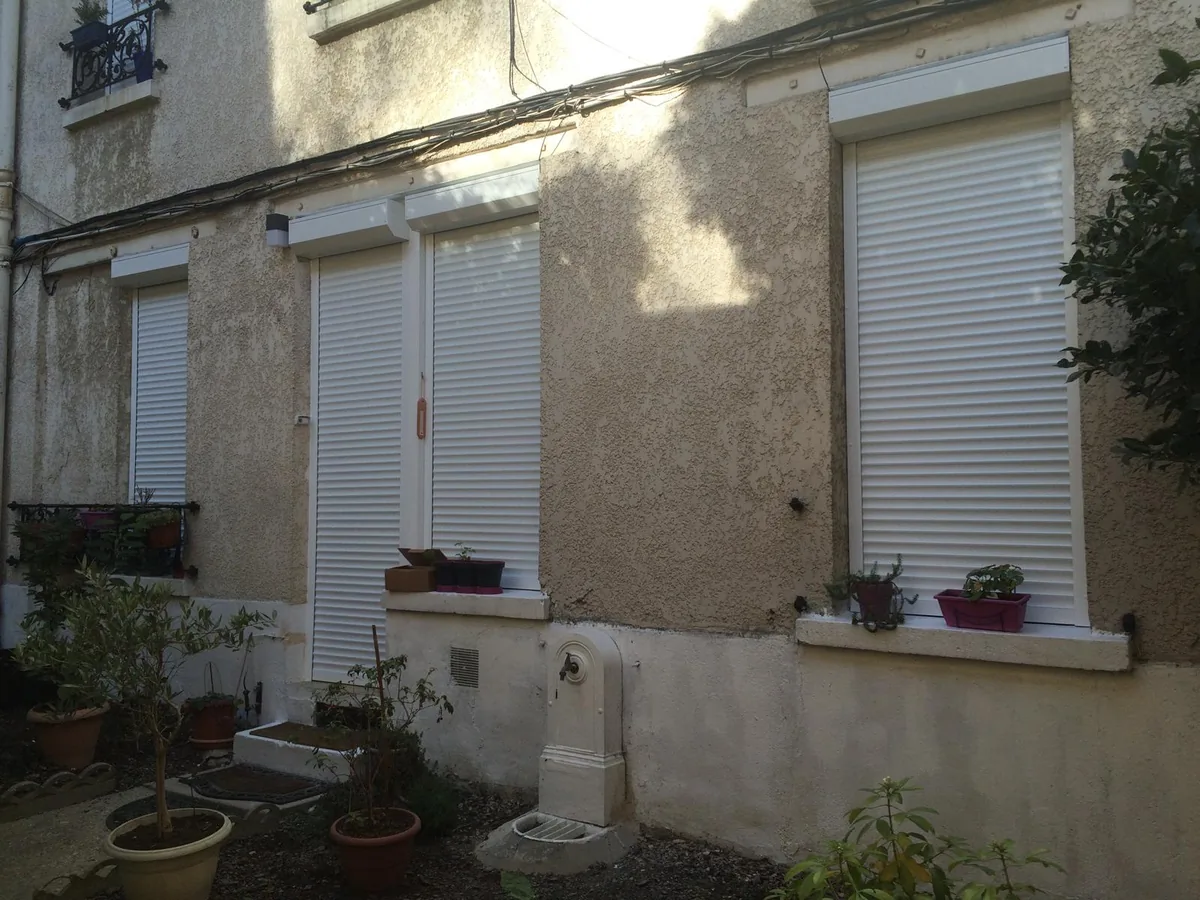Rez-de-chaussée d'immeuble avec volets roulants blancs aux fenêtres et à la porte-fenêtre