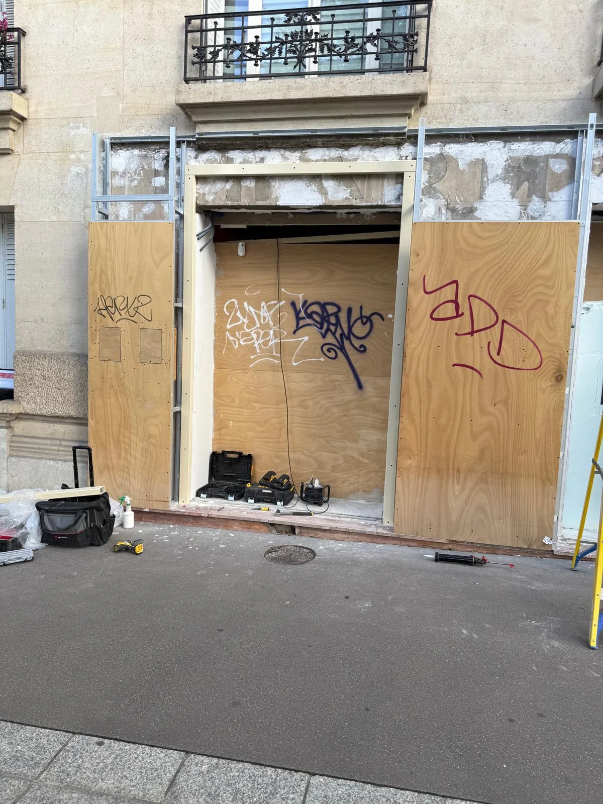 Devanture de commerce protégée par des panneaux de bois et un rideau métallique fermé, pendant des travaux