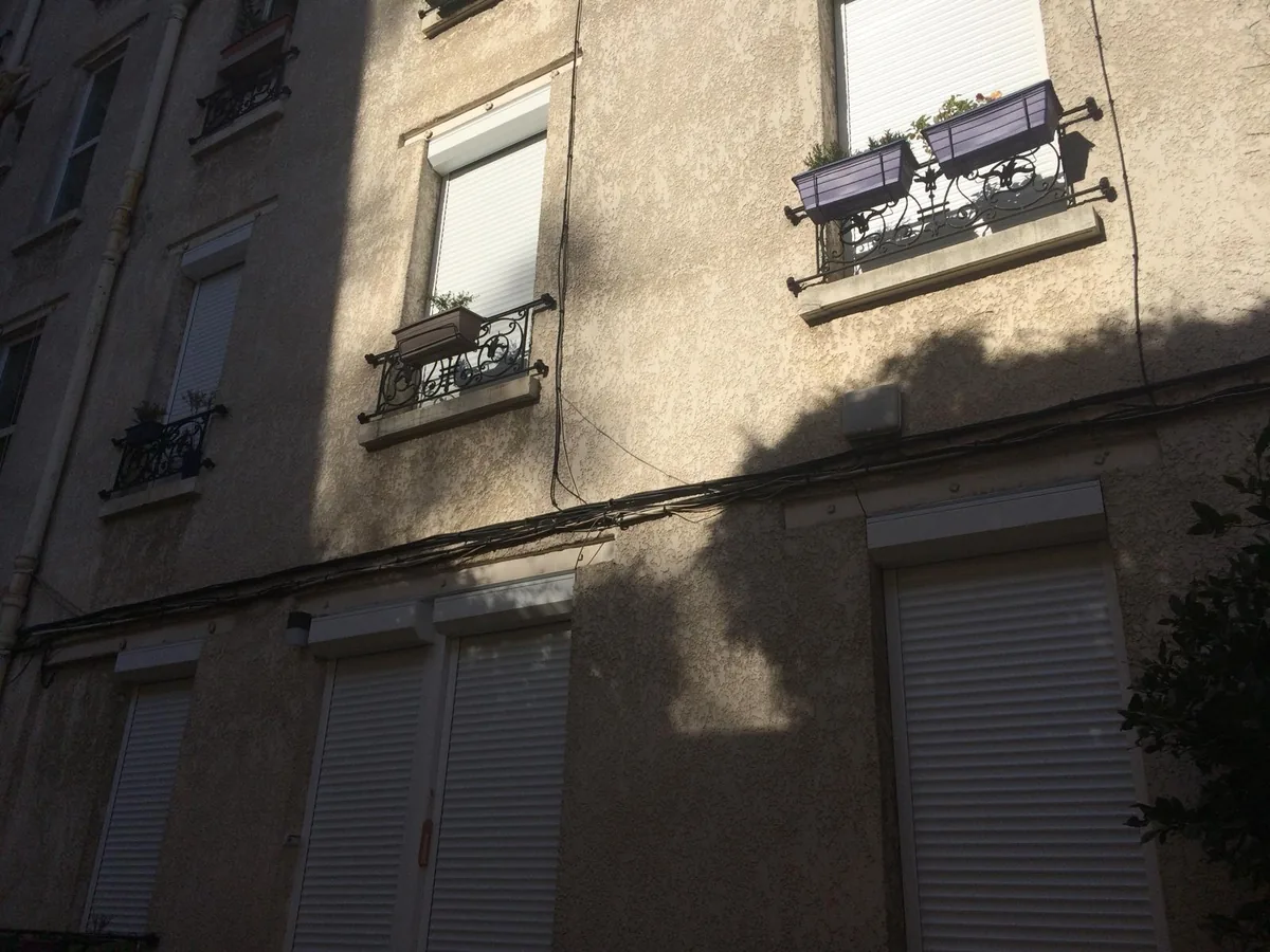 Façade d'immeuble avec volets roulants fermés au rez-de-chaussée, dans l'ombre