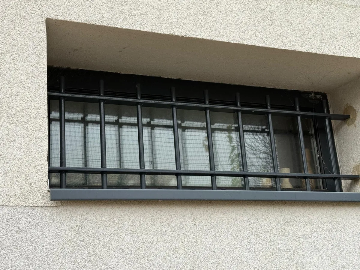 Grille de défense noire à barreaux posée sur une fenêtre de rez-de-chaussée