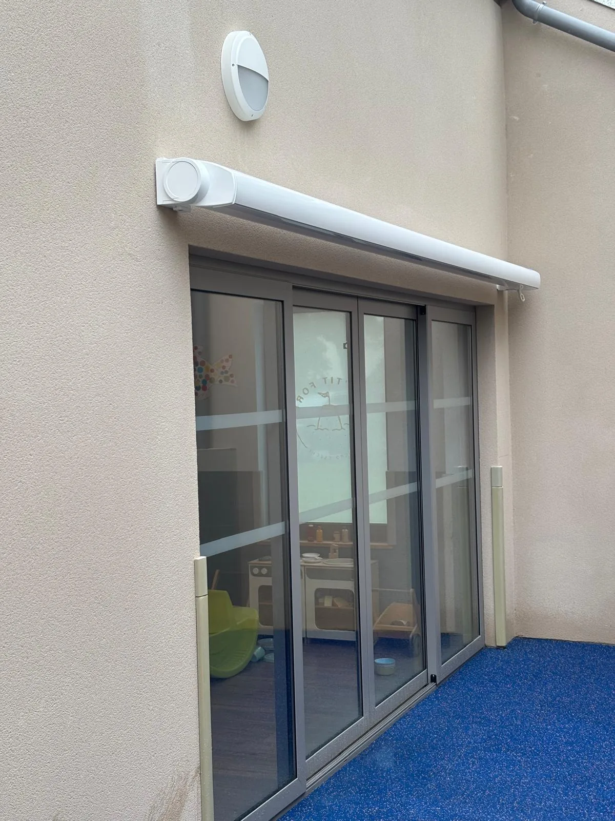 Coffre de store banne blanc fixé au-dessus d'une baie vitrée, sur une façade claire