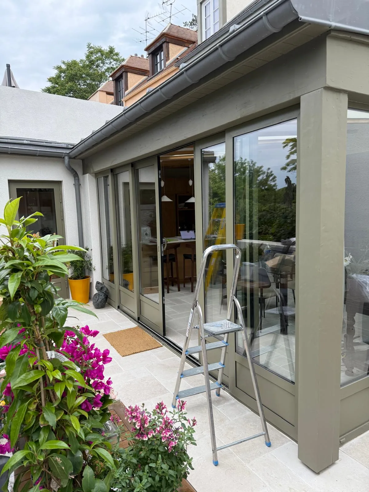 Véranda et terrasse fleurie d'une maison avec store, escabeau pendant la pose