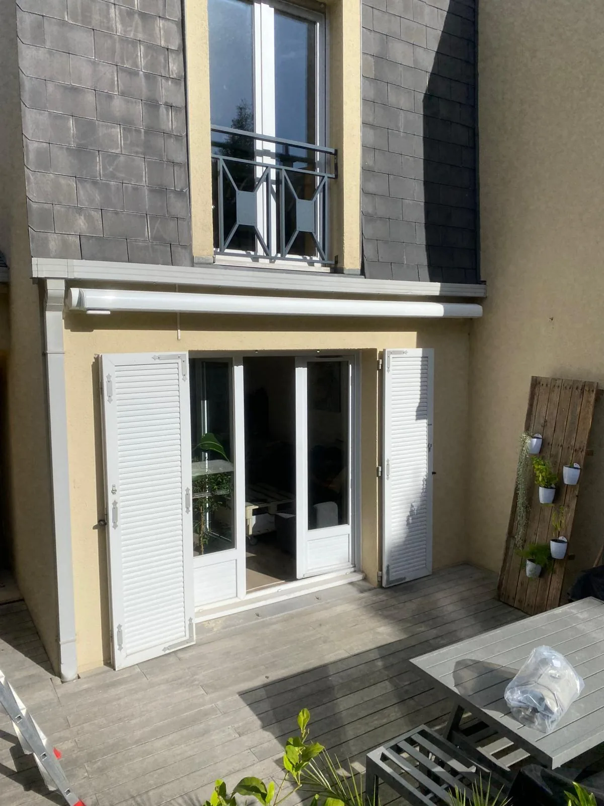 Maison de ville avec store banne gris au-dessus d'une porte-fenêtre et terrasse en bois
