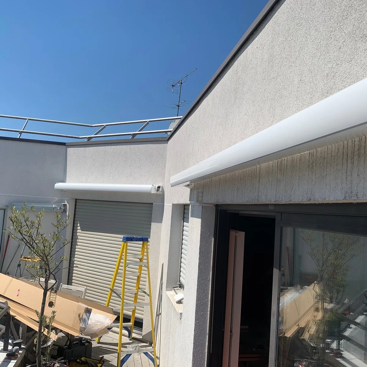 Store banne coffre blanc fixé en façade au-dessus d'une baie vitrée, vue en contre-plongée