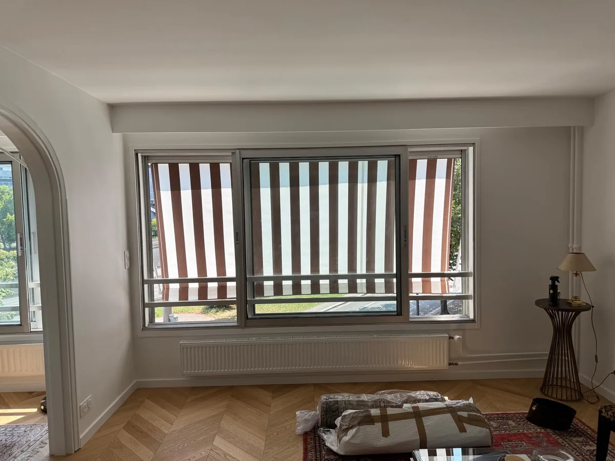 Stores corbeille rayés vus depuis l'intérieur d'un appartement, devant une grande fenêtre