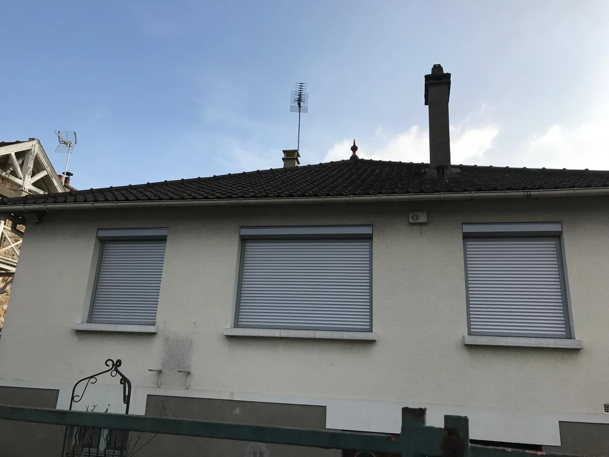 Façade de pavillon avec volets roulants gris fermés aux trois fenêtres