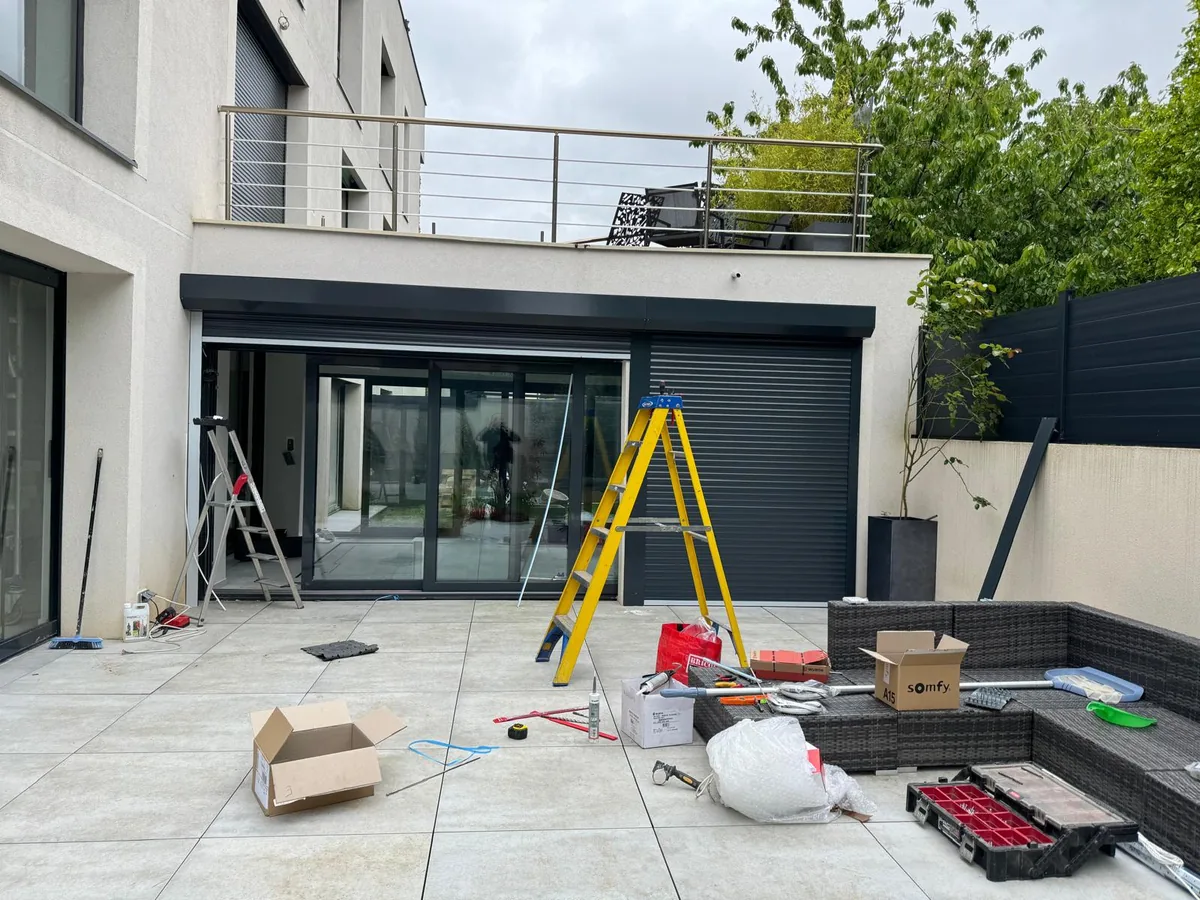 Grande baie vitrée de maison moderne équipée d'un volet roulant gris anthracite, terrasse en dalles