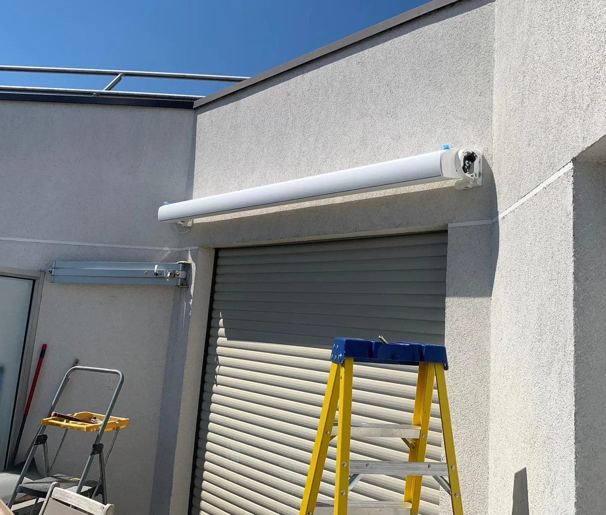 Store banne à coffre motorisé fixé en façade au-dessus d'un volet roulant