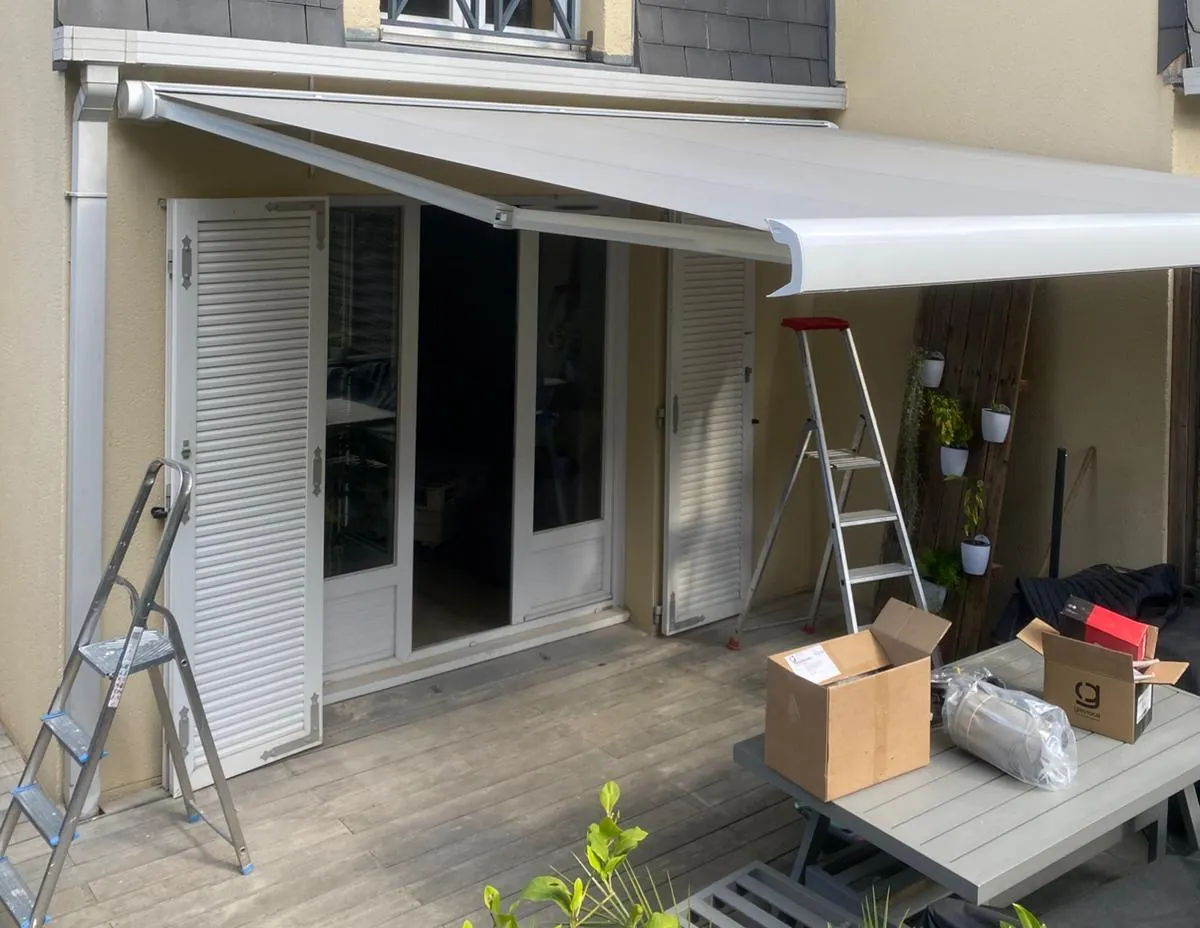 Store banne sur mesure posé au-dessus d'une porte-fenêtre à persiennes, chantier en cours