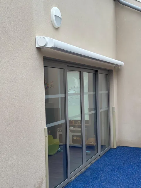 Coffre de store banne blanc fixé au-dessus d'une baie vitrée, sur une façade claire