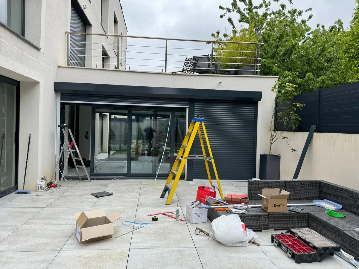 Grande baie vitrée de maison moderne équipée d'un volet roulant gris anthracite, terrasse en dalles