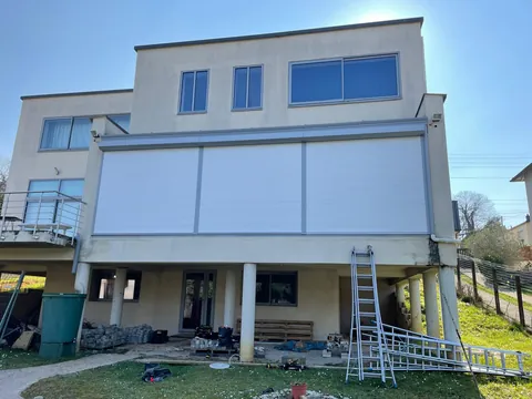 Maison sur pilotis avec grand store vertical de façade déroulé devant la véranda