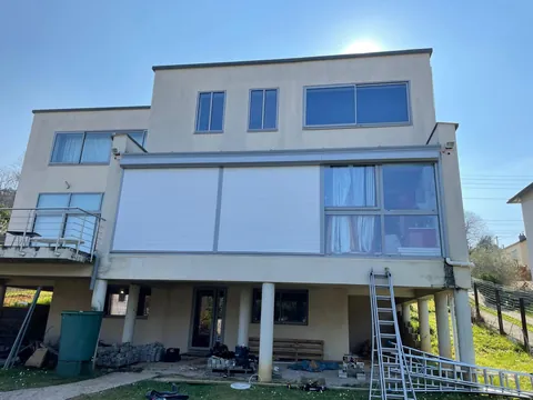Maison sur pilotis avec stores verticaux de façade partiellement déroulés devant la véranda