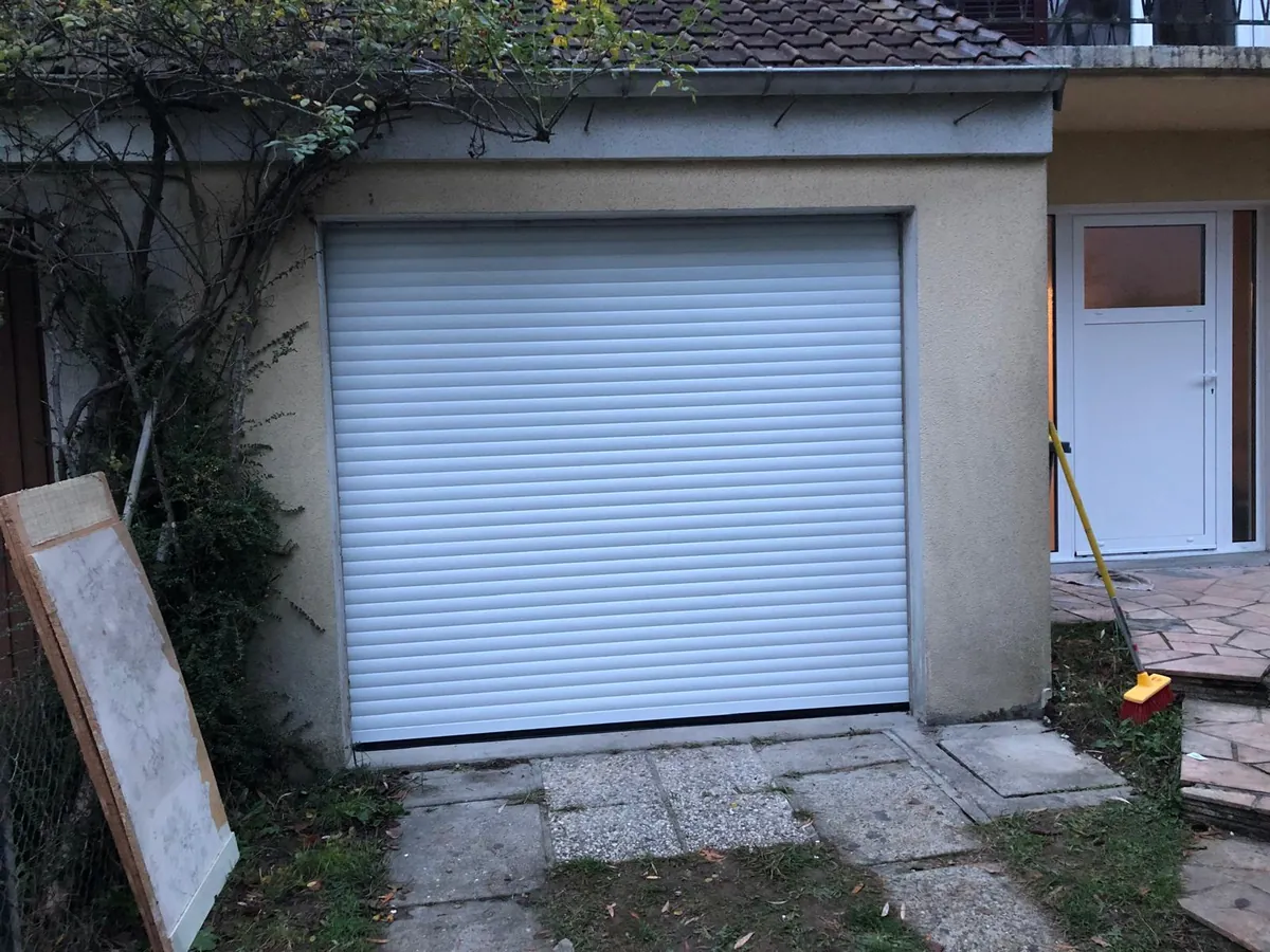 Porte de garage enroulable blanche posée sur un garage de maison, vue de l'allée