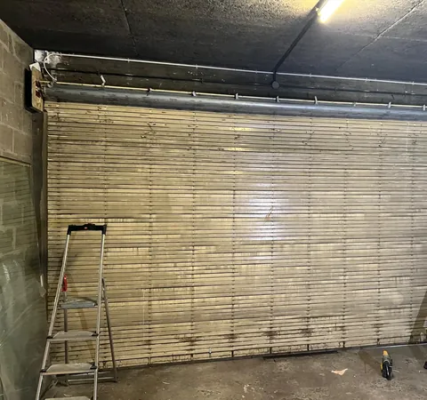 Rideau métallique à lames en cours d'installation dans un local, avec échelles